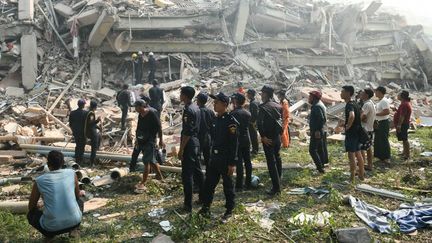 Des résidents de Mandalay (Birmanie) et des policiers assistent aux opérations de recherche et de secourisme le 29 mars 2025 dans des immeubles détruits par le séisme survenu la veille. (SAI AUNG MAIN / AFP)